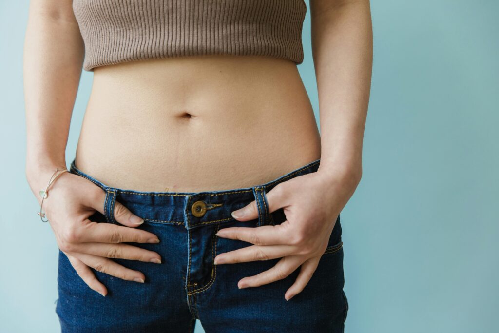 Close-up of a torso: person wearing a brown crop top and jeans, hands on the waistband of the jeans.