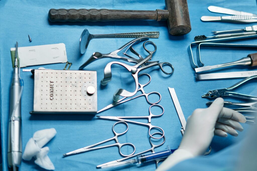 Surgical instruments laid out on a blue sterile tray, including scissors, clamps, scalpel, and a wooden mallet.